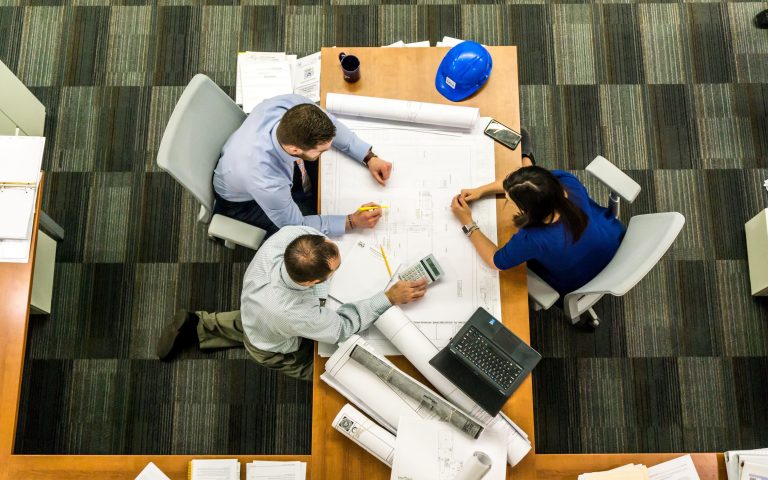 three people at meeting table construction hat